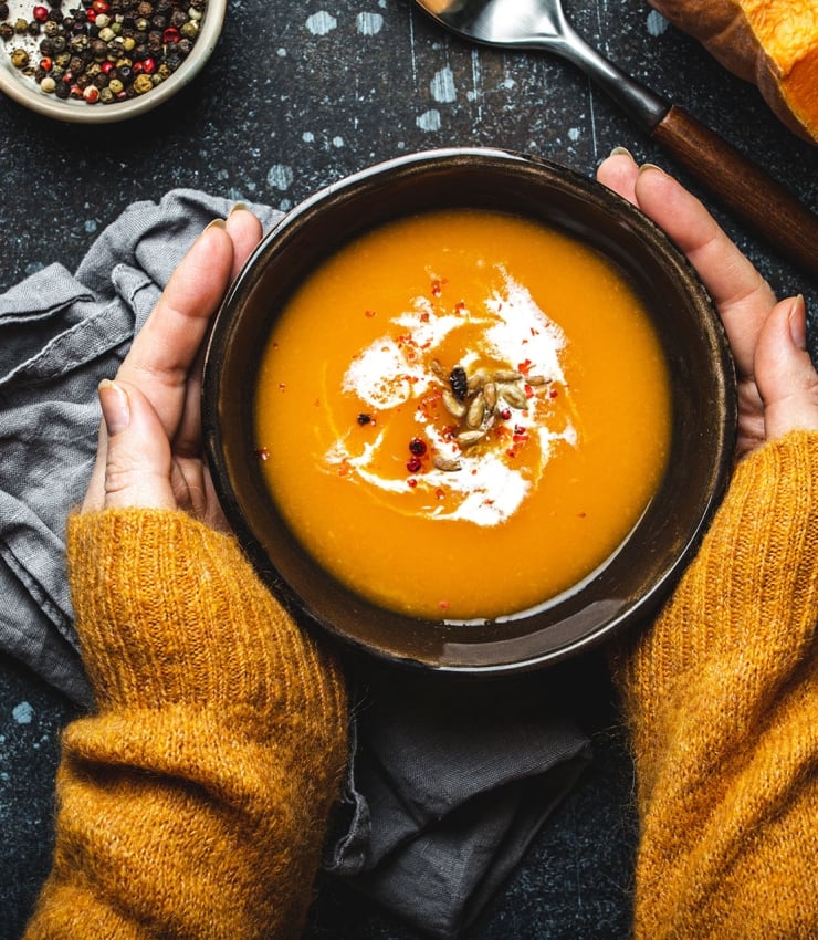 hands holding a bowl of pumpkin soup