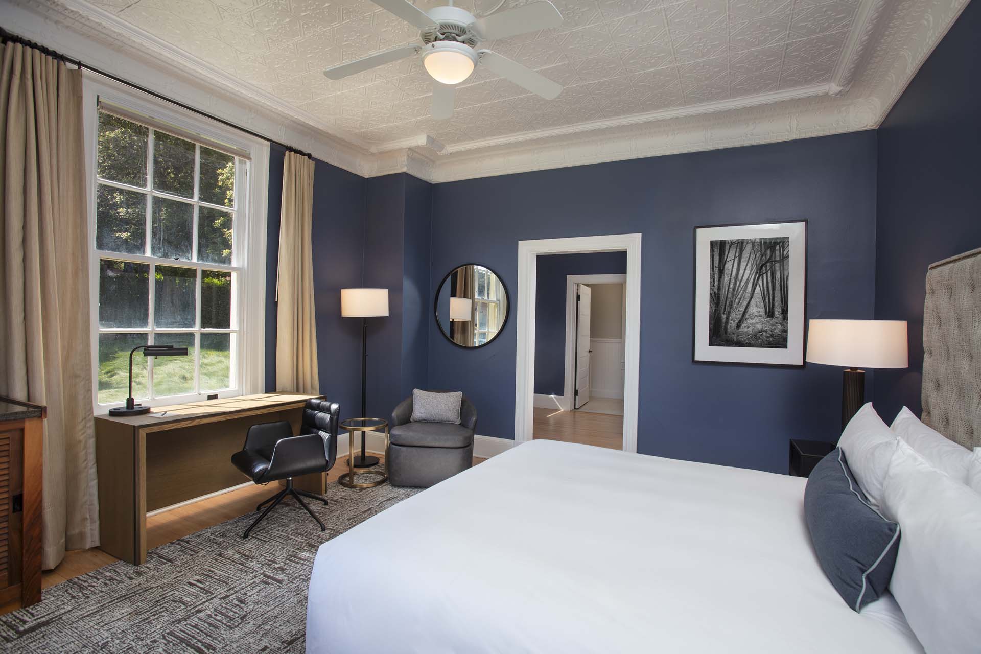 Guestoom with King bed, desk and chair, sitting chair and view outside of the grass