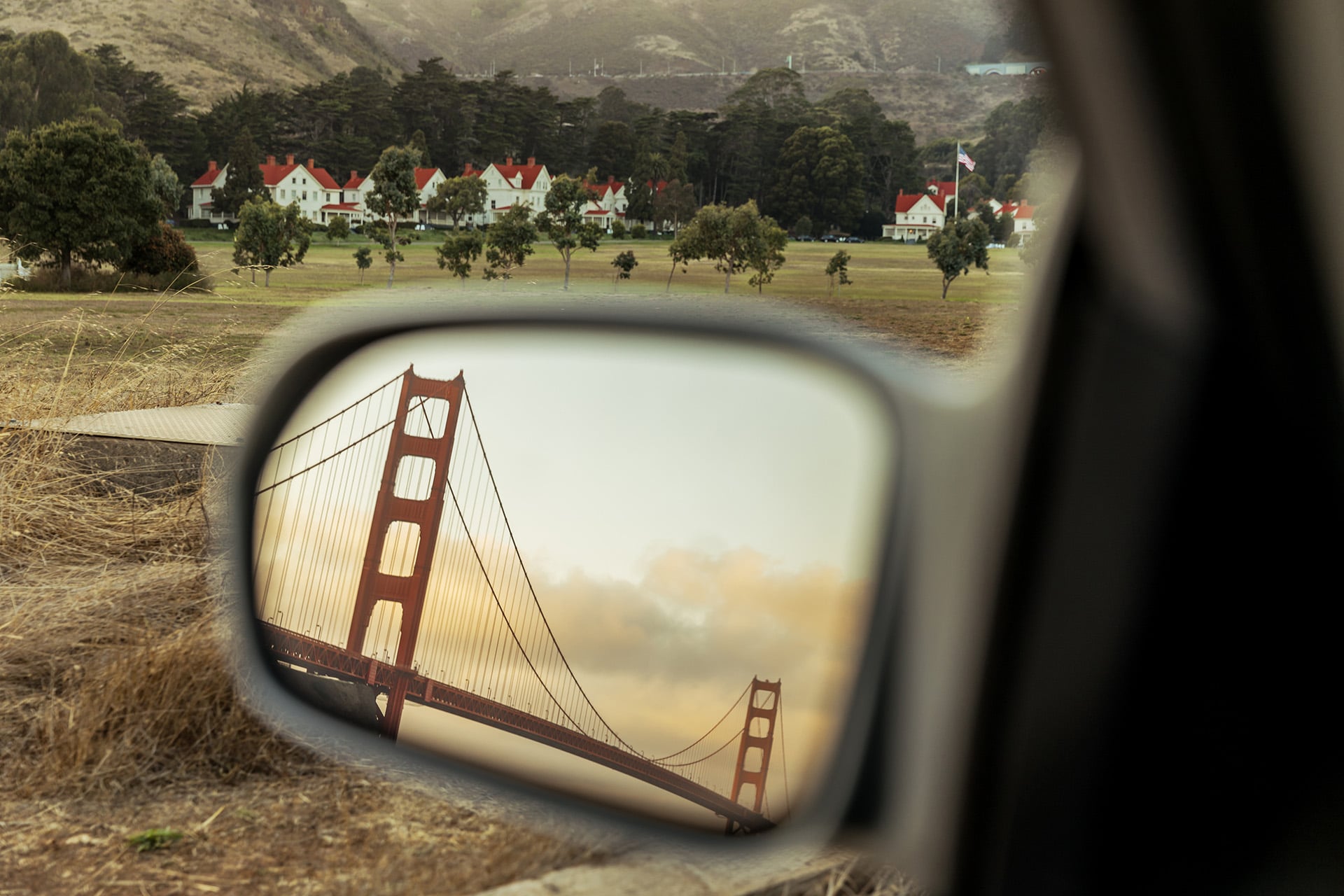 car's side mirror with Golden Gate Bridge in the side mirror and cavallo point buildings in the distance