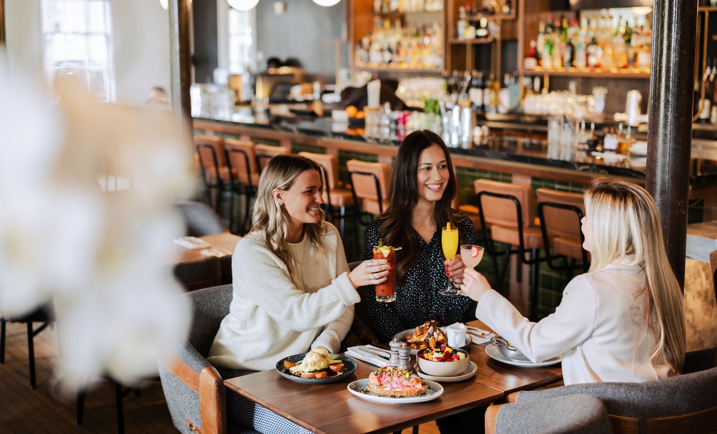 3 women sharing drinks and food at a bar