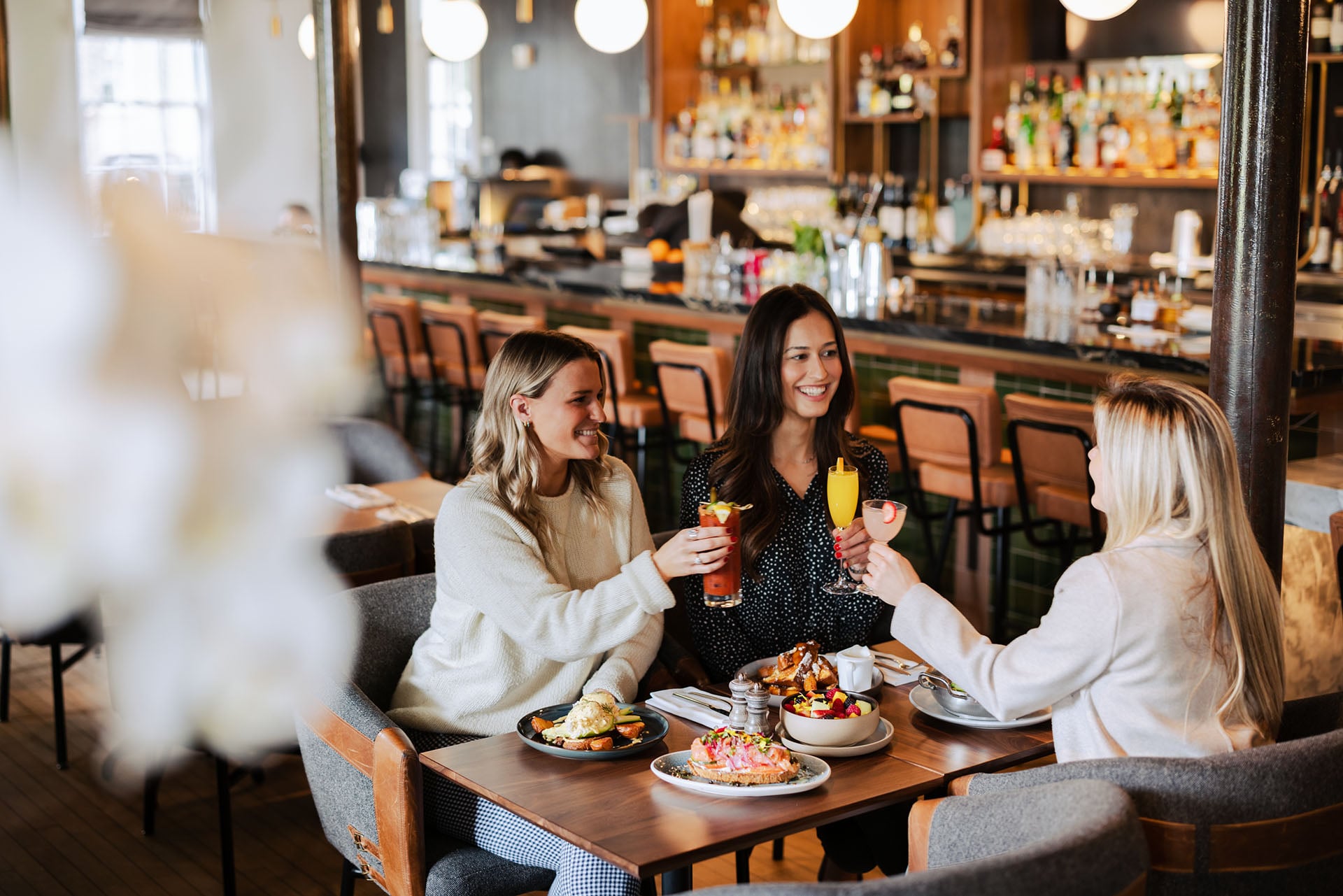3 women sharing drinks and food at a bar
